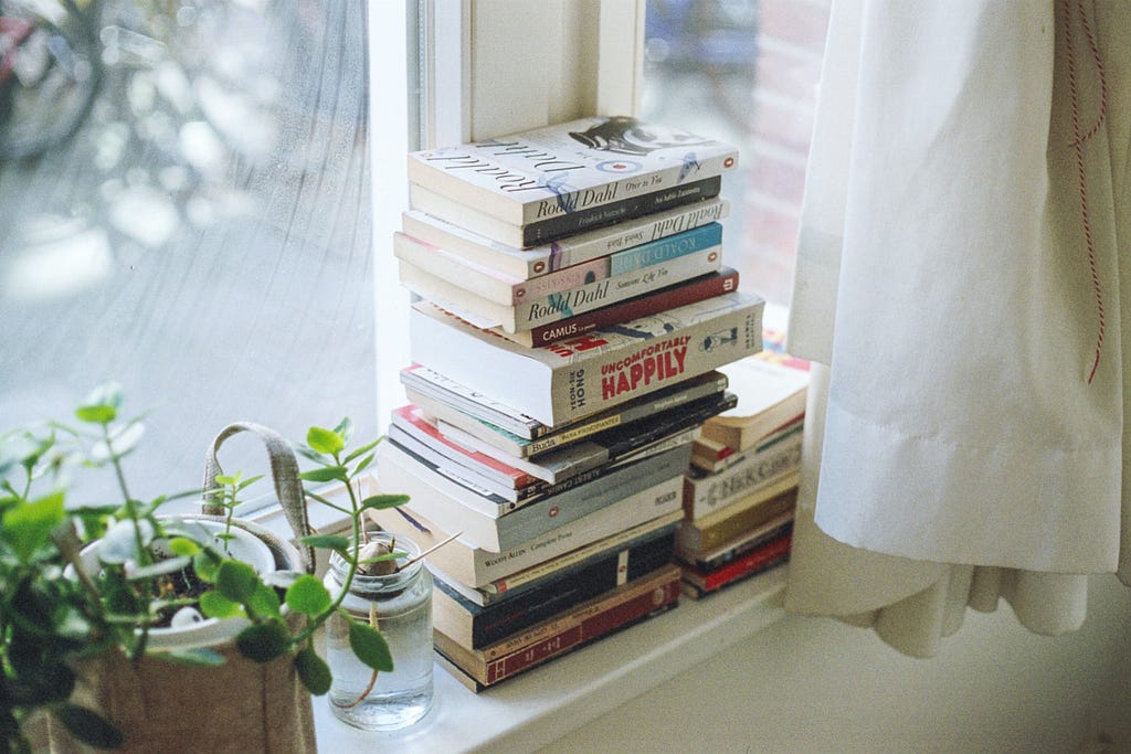 A stack of books by a sunny window.