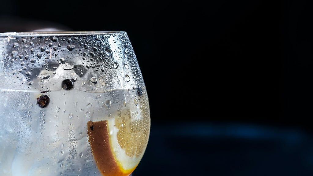 Gin and tonic in a glass with lemon and juniper berries against a dark backdrop.