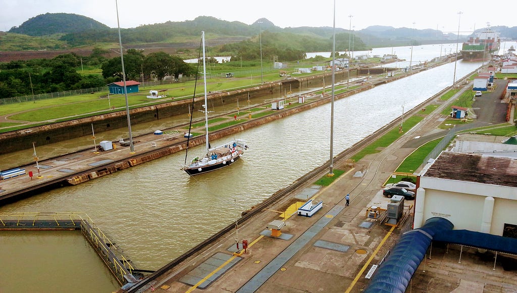 Photo showing a small yacht and a large ship entering the Miraflores Locks, Panama Canal