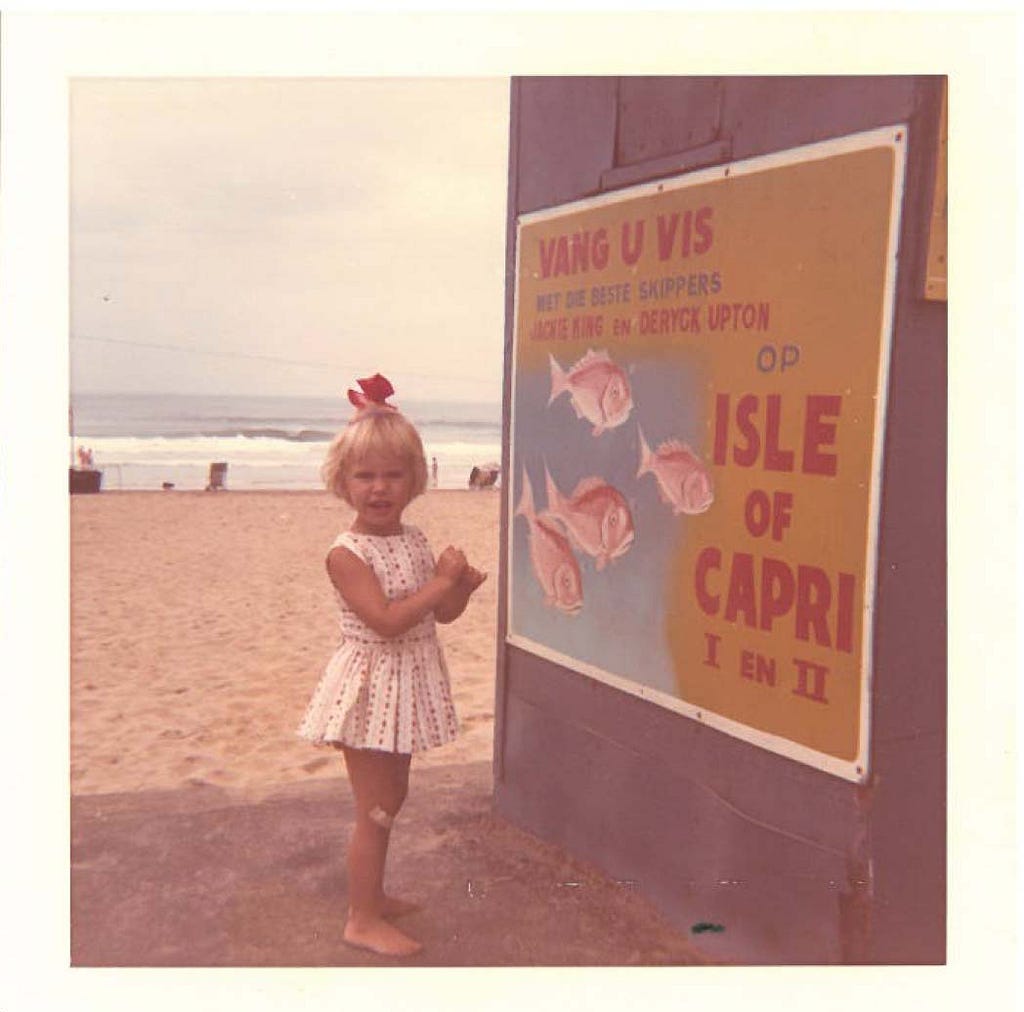 A young female child standing next to an Isle Of Capri sign with the sea in the background