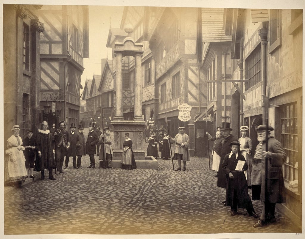 Black and white photo showing cobbled street with Tudor-style houses and a couple of dozen men and women in period costume.