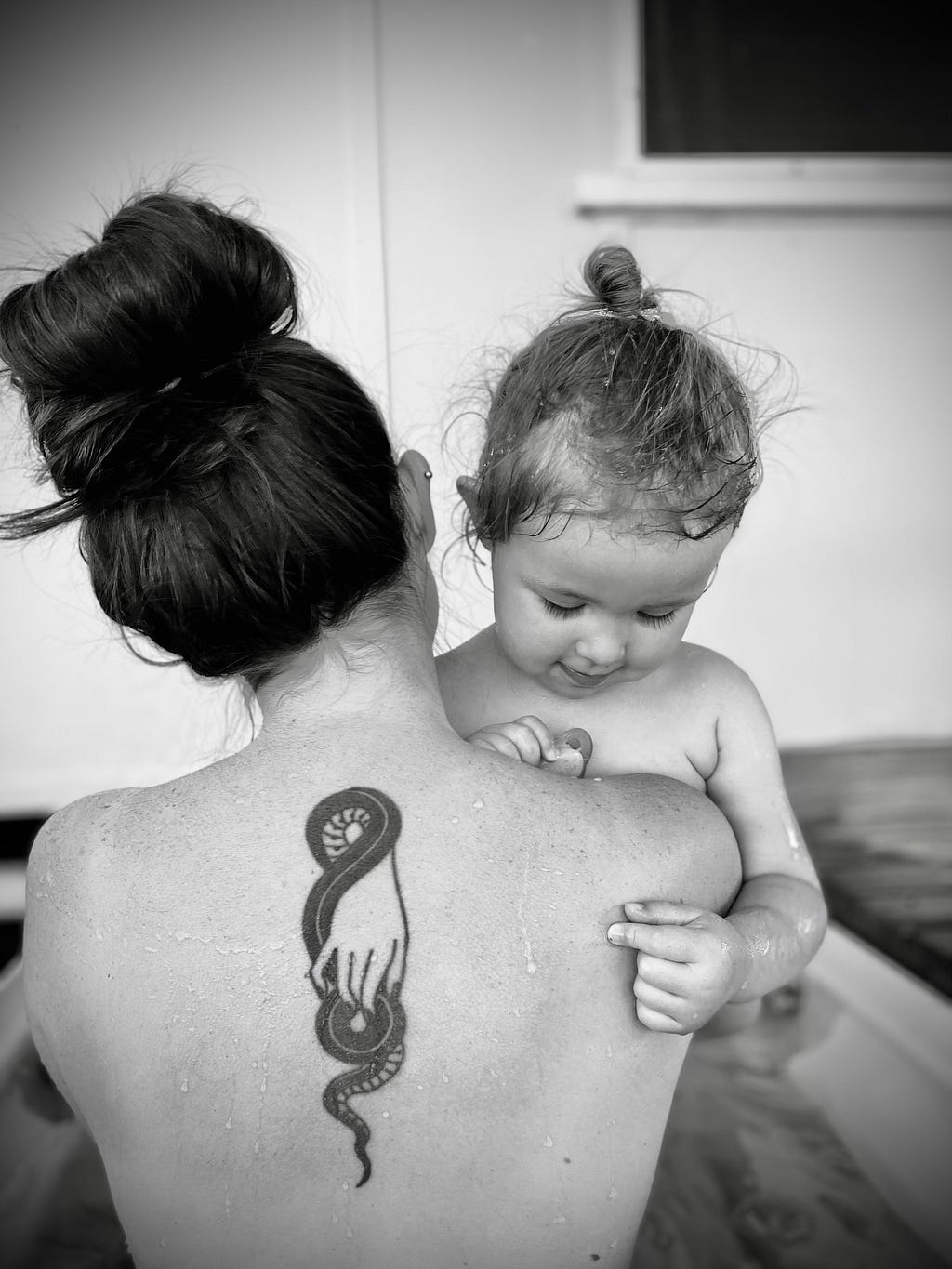 A black and white photo of a mother and her daughter embracing in a bathtub