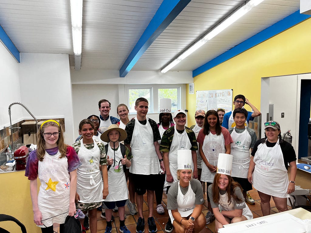 campers and staff stand around each other and smile at the camera while wearing aprons