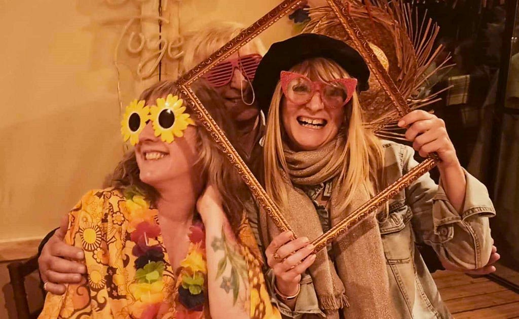 Three smailing people dressed up in hats and sunglasses a photobooth