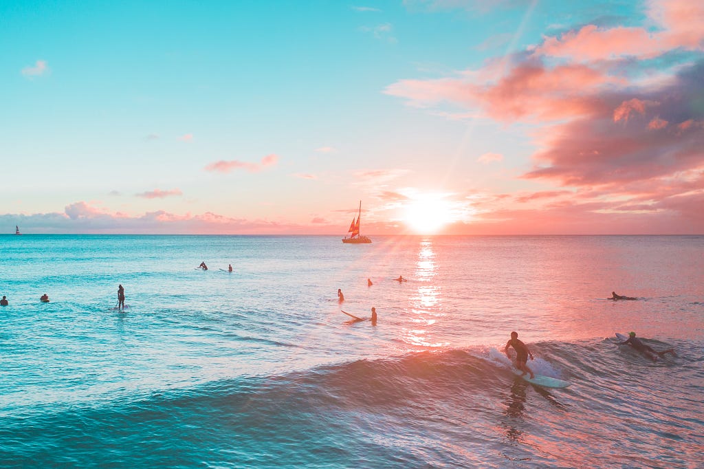 Sunset over a Hawaiian beach with surfers, paddle surfers and a boat.