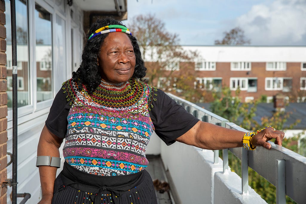 A woman standing outside on a balcony with a intricate colorful shirt