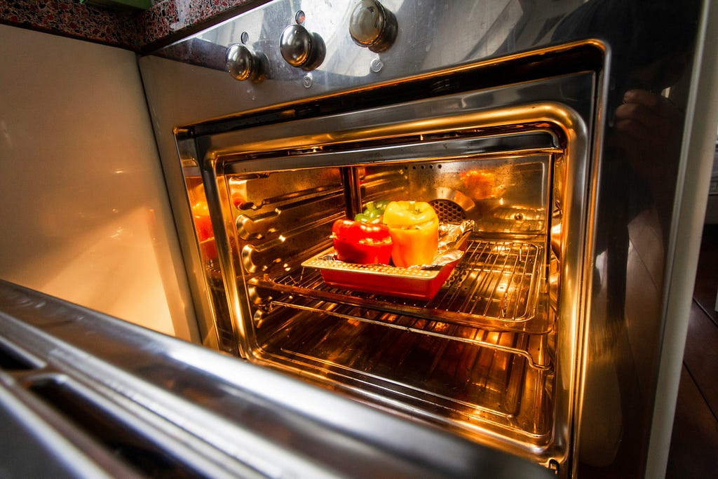 Closeup image of an open microwave oven — inside there is a baking dish holding stuffed bell peppers.