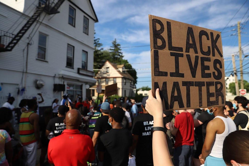 Photo of a crowd of protesters in New Rochelle, with person in foreground holding up a Black Lives Matter sign