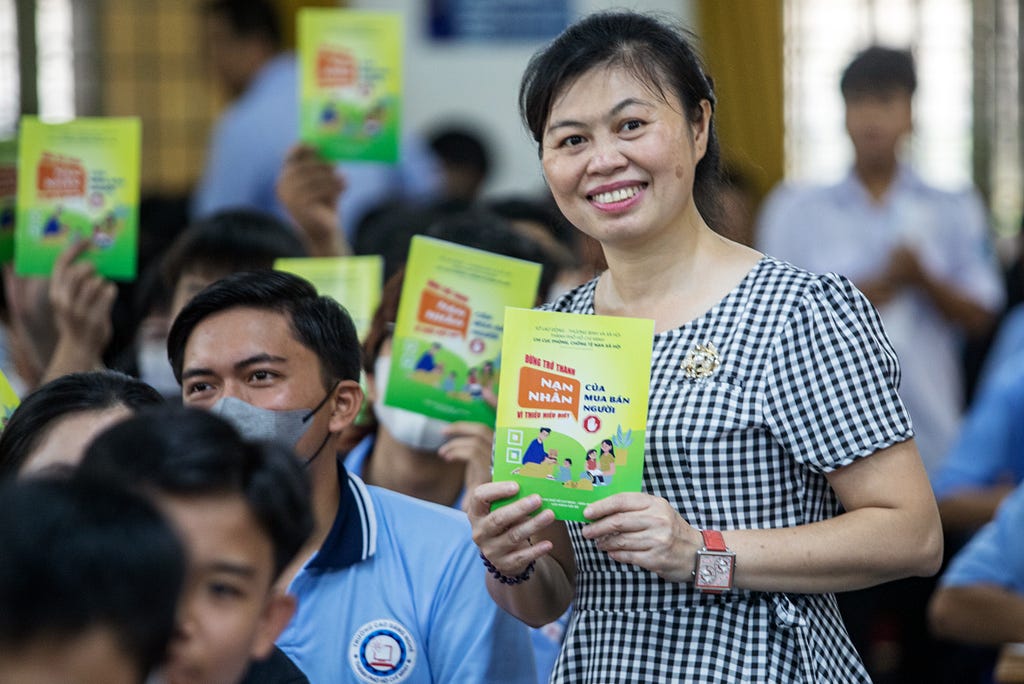 A woman smiles while holding a small book and surrounded by other people holding the same book aloft.