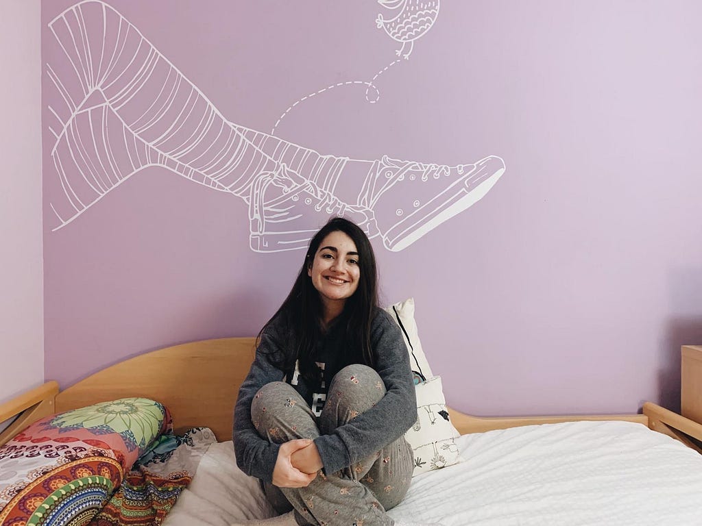 Miriam sitting on her bed with a purple wall behind her