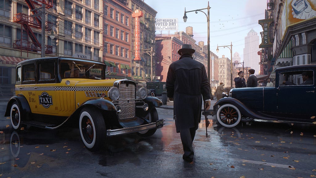 A screenshot from Mafia: Definitive Edition, featuring an unknown man in a jacket holding a tommy gun in his right hand on a street.