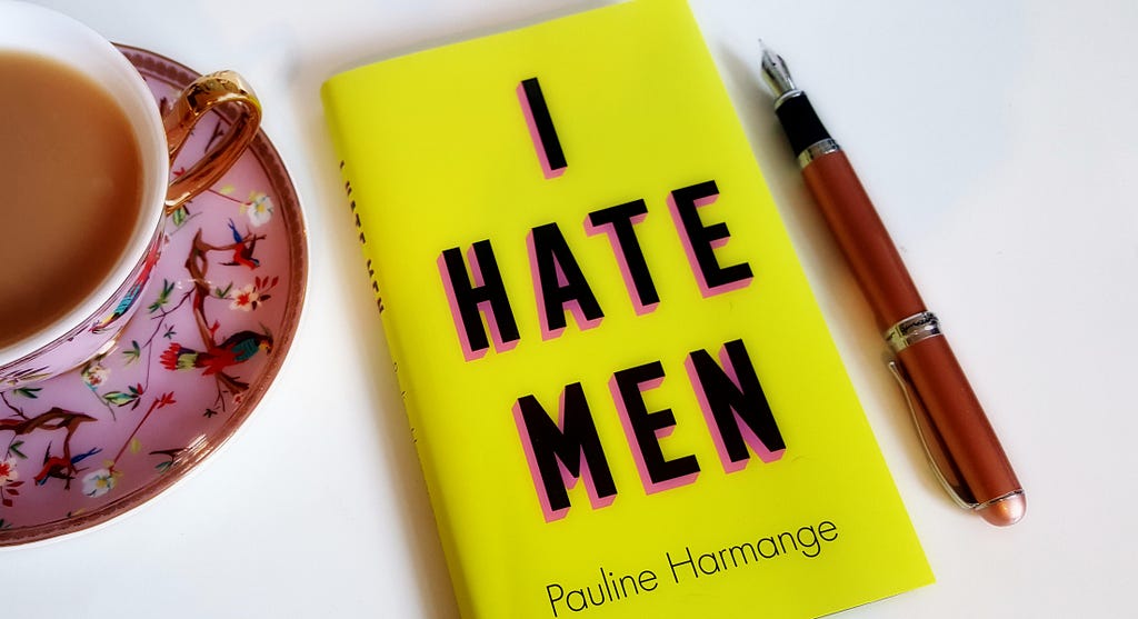 “I Hate Men” book laying on a desk next to a cup of tea and a pen.