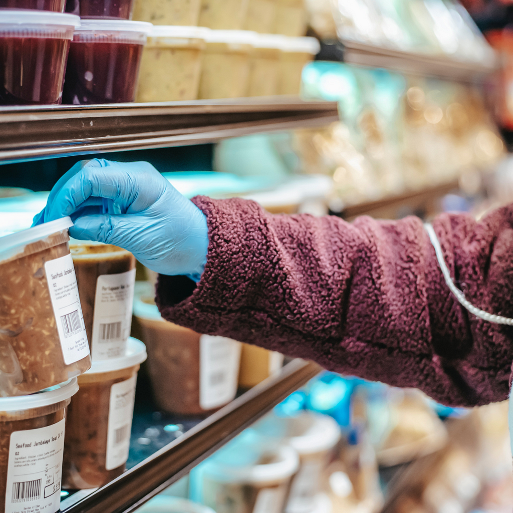 Person looking at a deceptive food label in a grocery store while wearing blue plastic gloves
