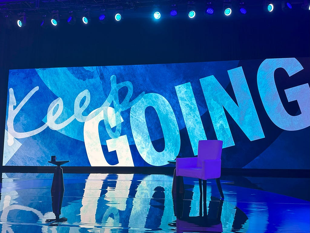 The empty stage at CGI23. The words on the blue screen read “Keep Going.”