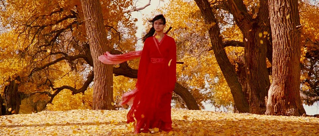 Mulher com roupa tradicional chinesa na cor vermelha com árvores de folhas amarelas ao fundo.