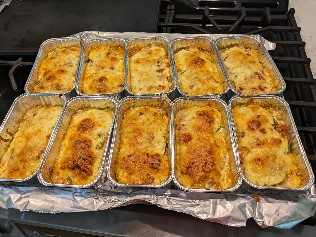 10 single-serve aluminum tins containing zucchini lasagna and topped with golden-brown cheesy goodness