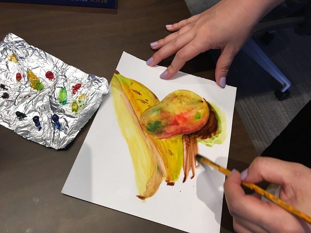 Closeup of a person’s hands painting bananas and a pear in watercolors