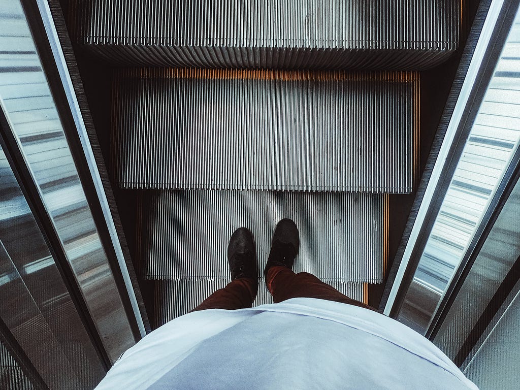 Person riding escalators looking down at own feet