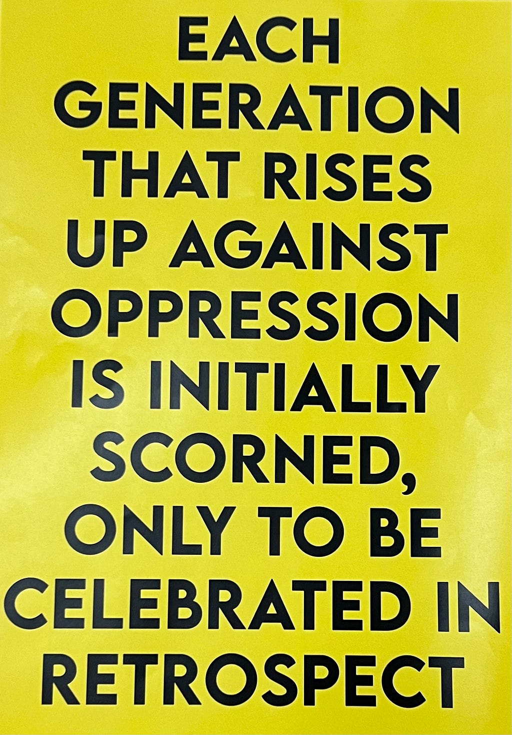 Picture of yellow poster with black text that reads: each genderation that rises up against oppression is initially scorned, only to be celebrated in retrospect.