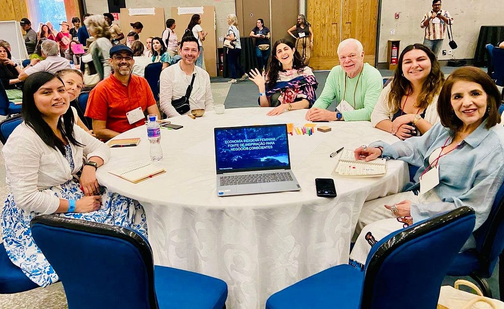 Eight people sit at a roundtable with an open laptop.