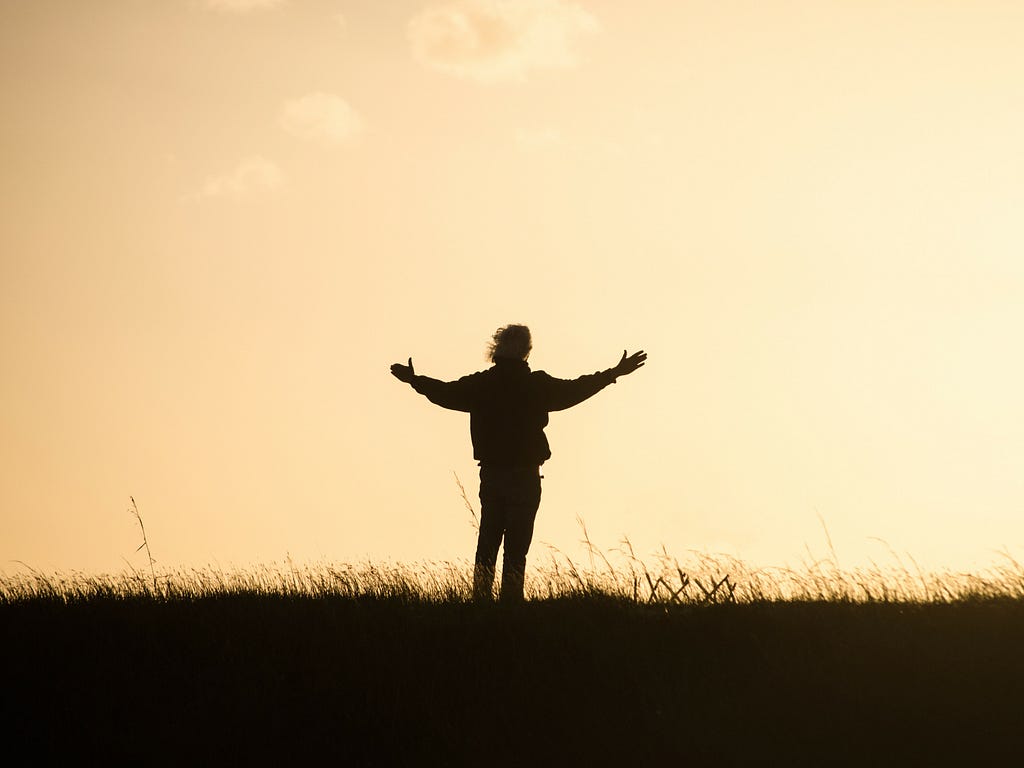 A person standing in a field, with his arms wide open.