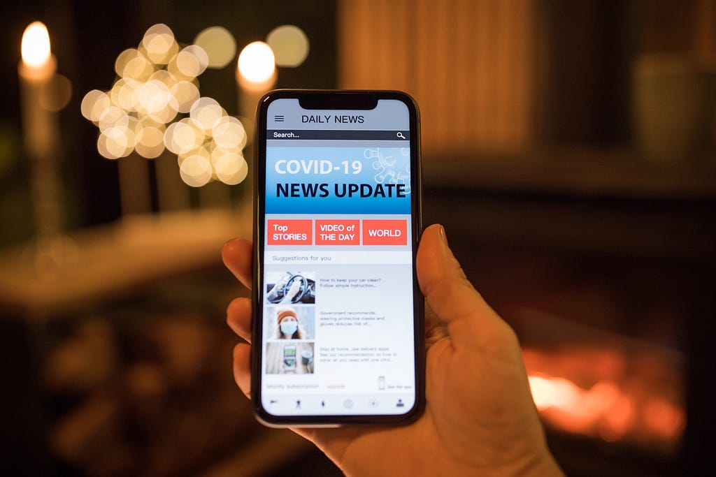 A hand holding a cell phone with a COVID-19 news update on the screen. Photo by svetikd/Getty Images