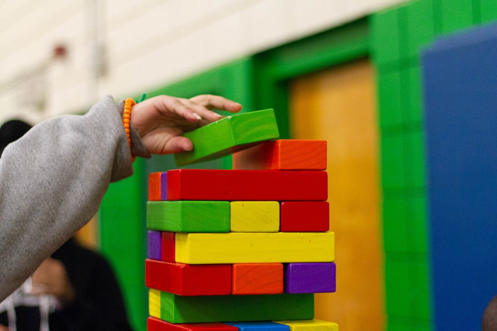 A hand placing a green block on a colorful jenga tower.