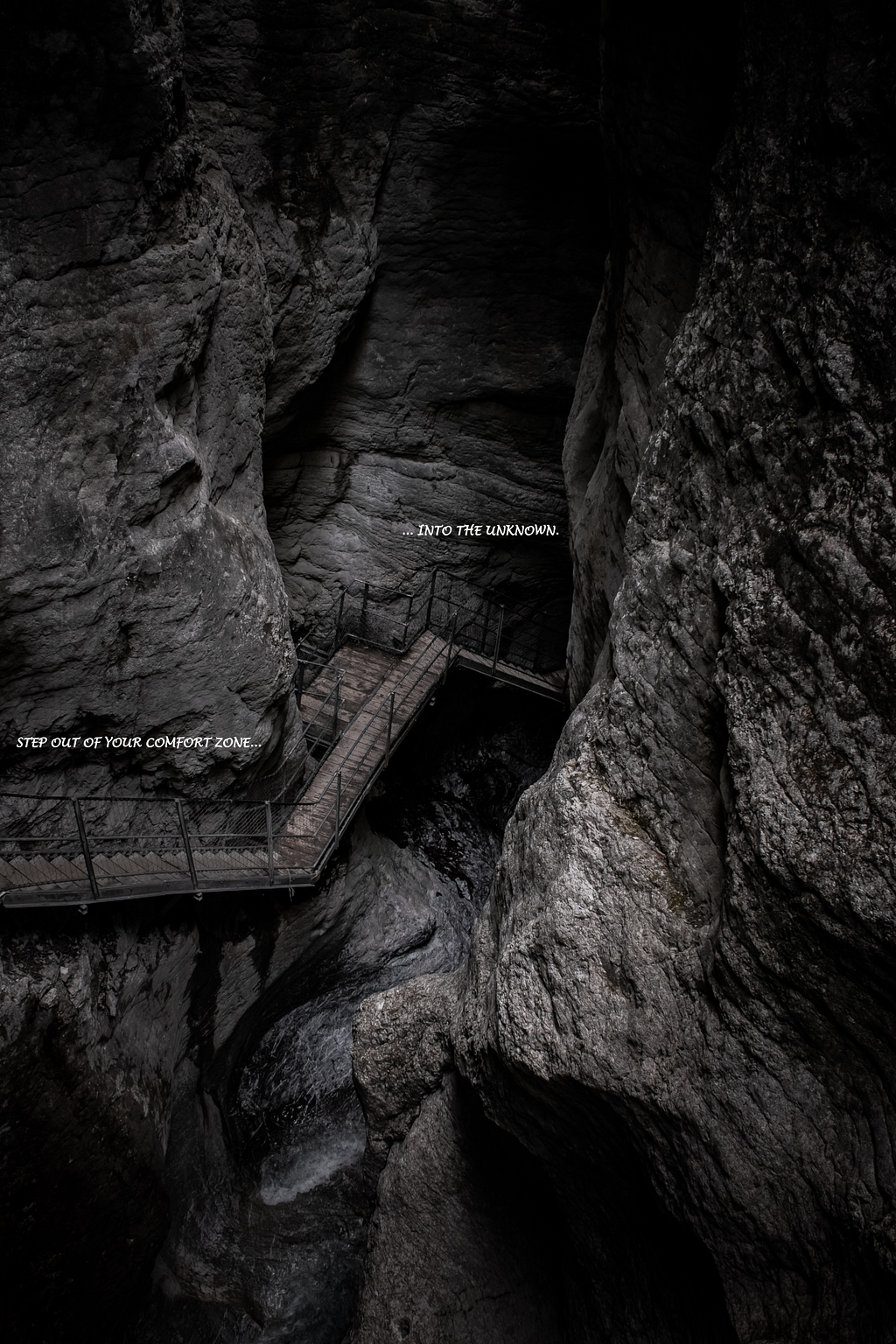 Photo of a wooden staircase with metal guard rails going down several levels into inside a rock formation with caves. The staircase leads to a dark cave. The text on the photo says “Step out of your comfort zone and into the unknown.”