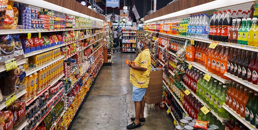 Shopper standing between two fully-stocked isles of goods in a supermarket