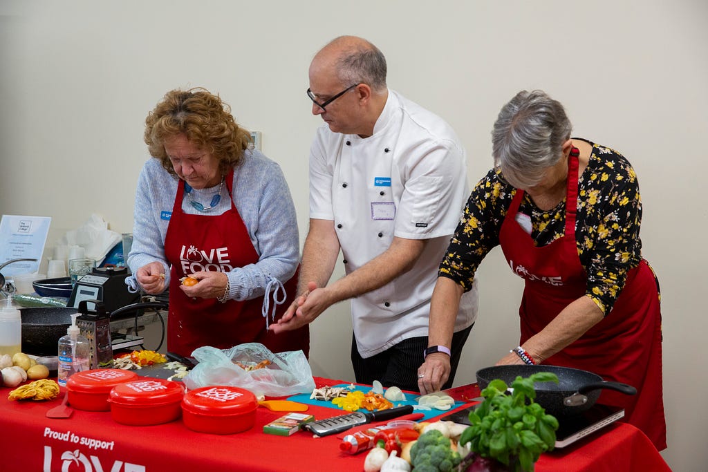 Three people preparing vegetables on a table with a red table cloth branded Love Food Hate Waste