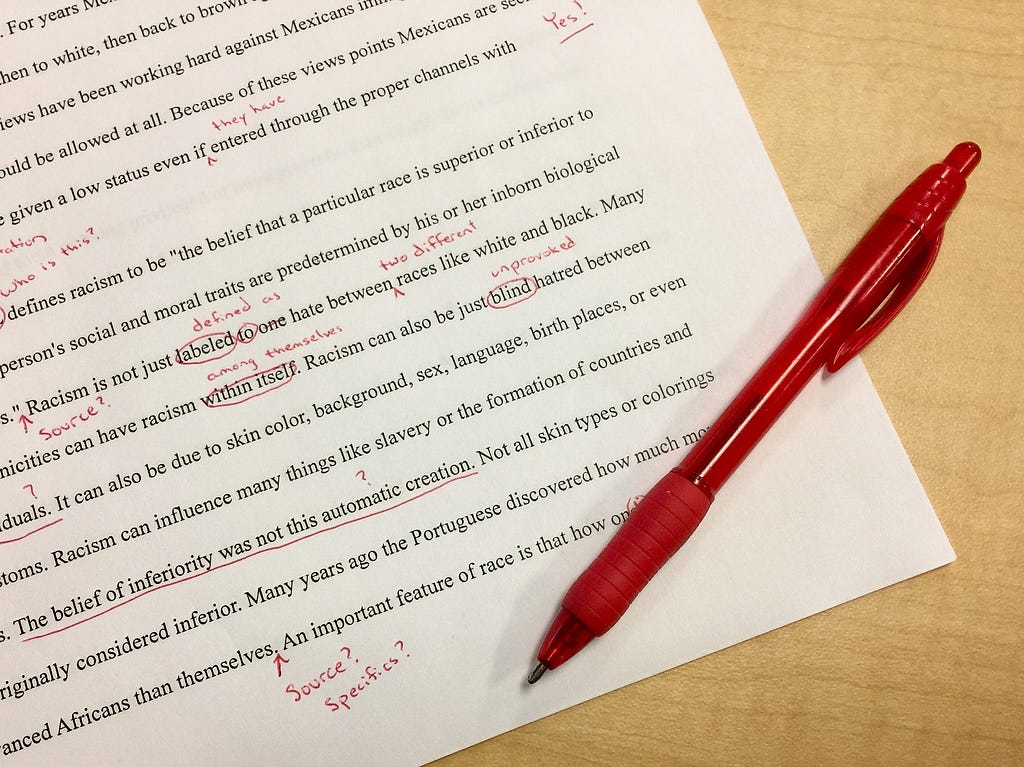 A typed piece of white paper with red ink edits scribbled on it. A red pen lays across the page.