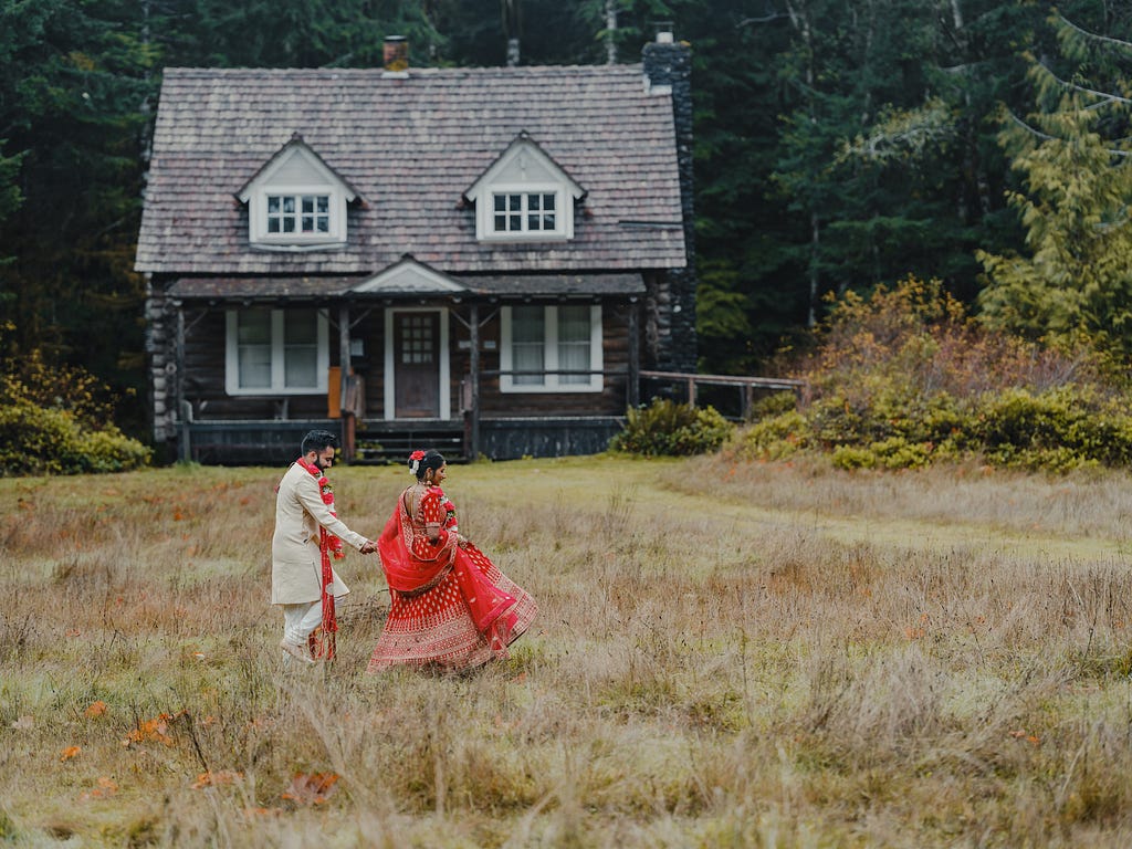 Young Indian couple in traditional sagai attire, walking past old house in Pacific Northwest