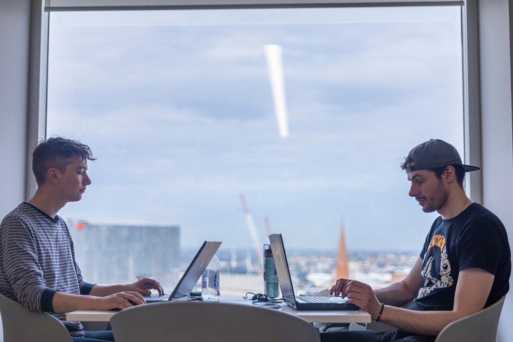 Photo of two participants on their laptops against the backdrop of the Melbourne cityscape
