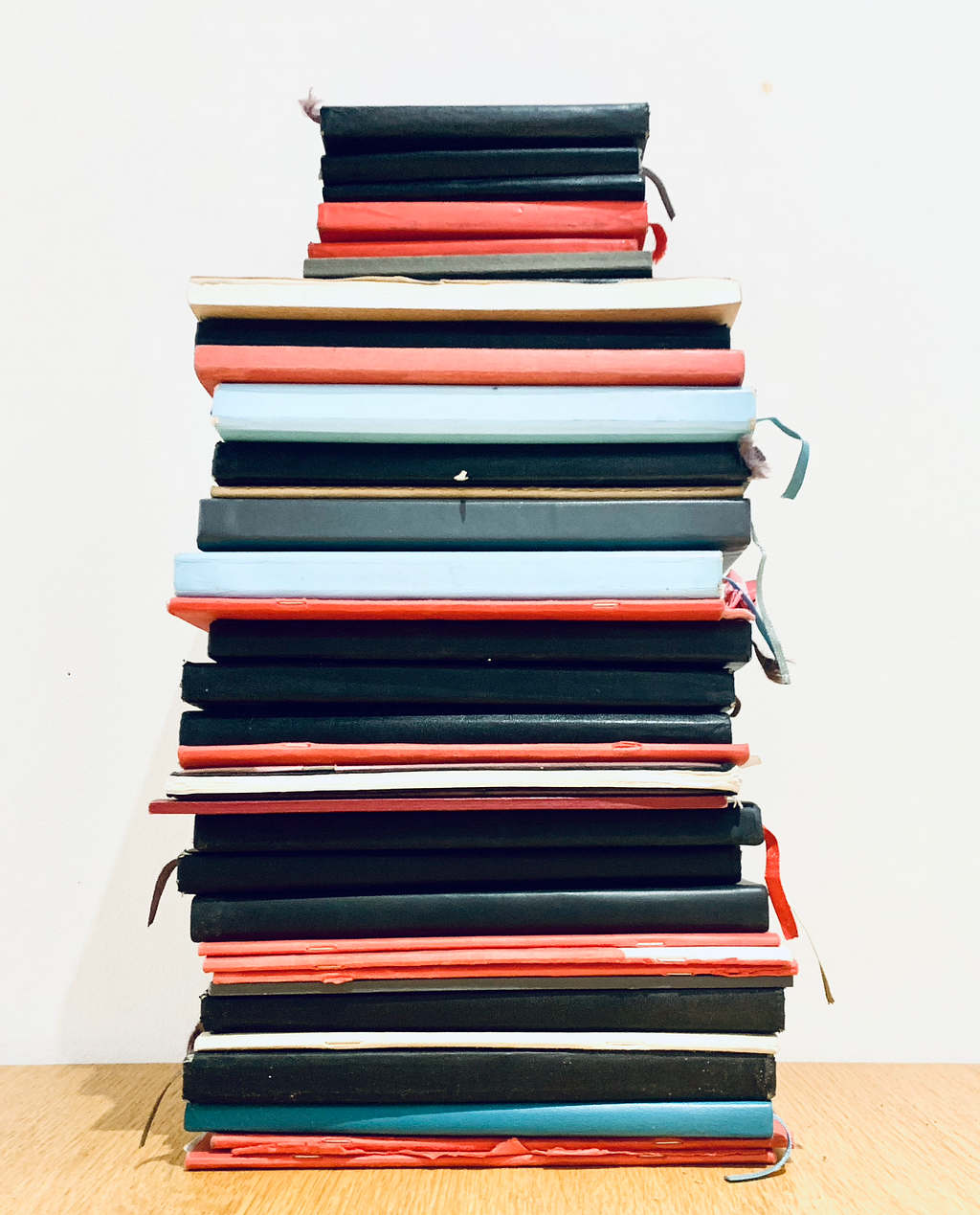 A stack of sketch books piled up in red, black and sky blue
