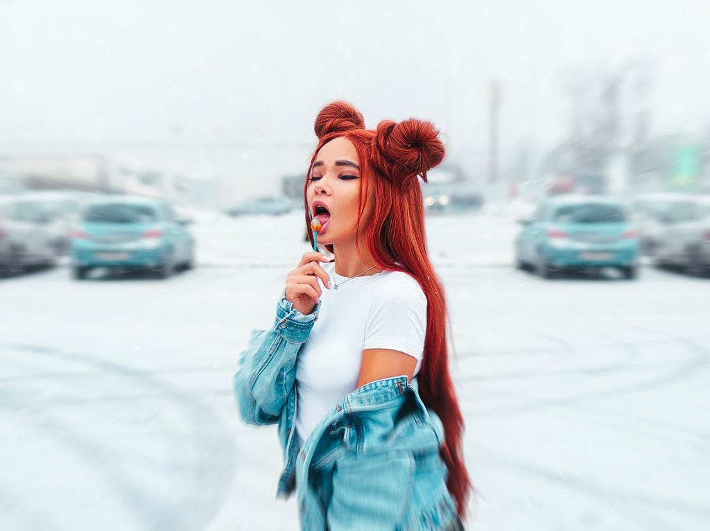 A woman in a denim jacket with red hair licking a lollipop standing in a carpark. Photo: Andrey Zvyagintsev on Unsplash