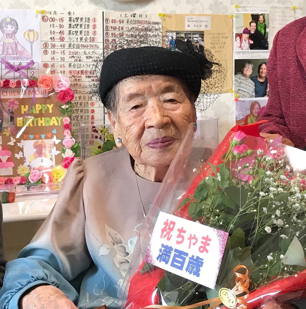 A nicely dressed elderly woman holding flowers.