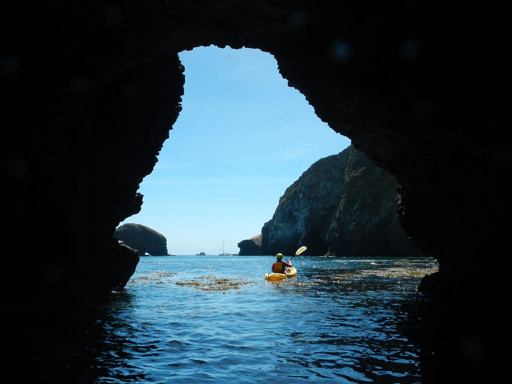 A kayaker on a guided trip paddles through a natural tunnel east of Scorpion Harbor on California’s Santa Cruz Island in Channel Islands National Park. (copyright April Orcutt — all rights reserved)