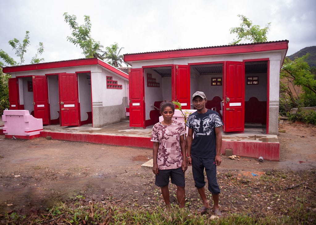 A man and woman stand outside of a station of colorful latrines that have been built to be accessible to all.