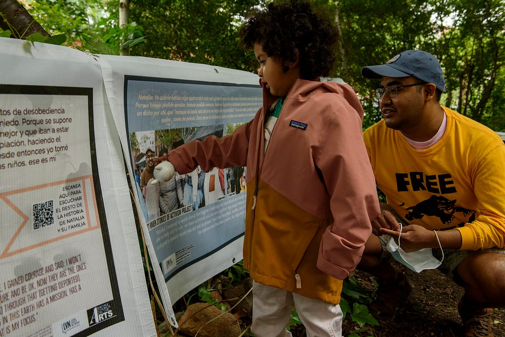 A child points to a picture of his father, on one of the banners hanging in the park