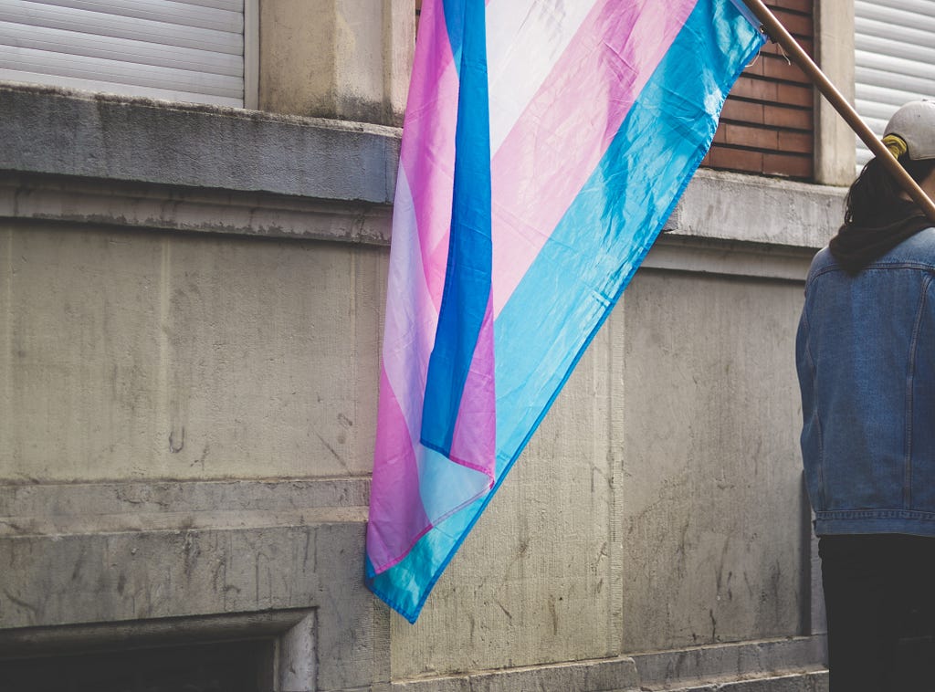 A person holding a transgender pride flag next to a building