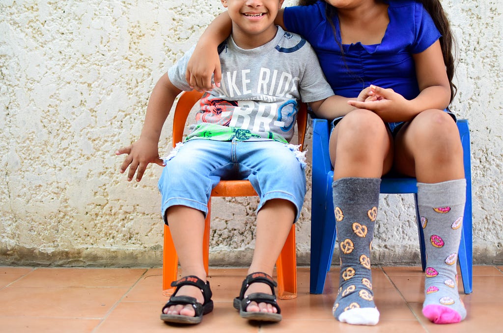 Niño de 5 años con su hermana, sentados. Ella usa medias impares.