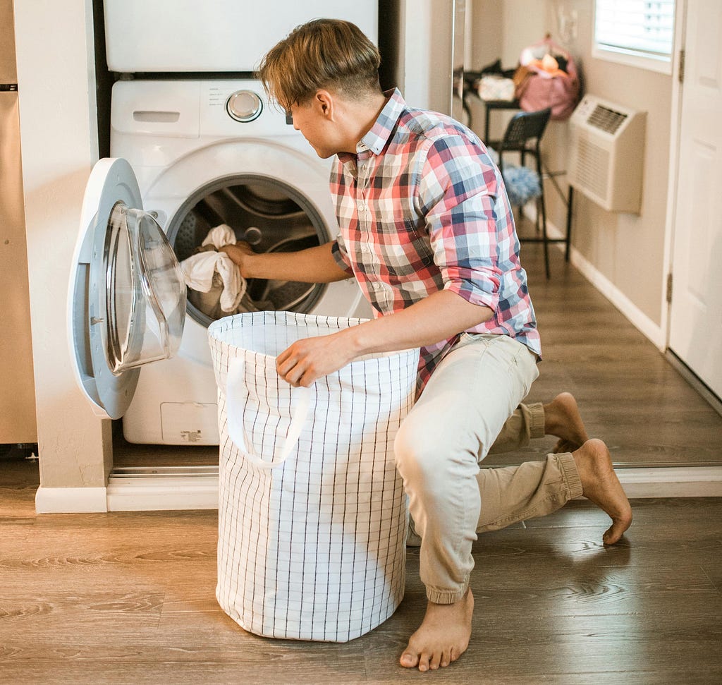 A man in a plaid shirt loads clothes into a laundry machine.