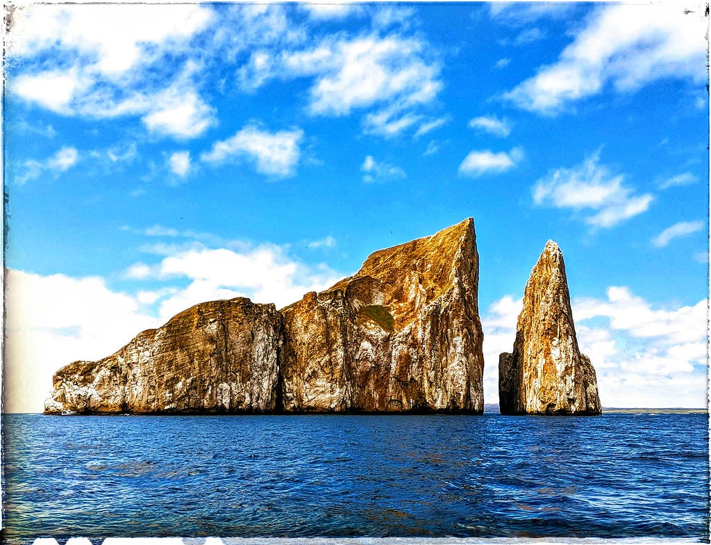 Two white-frosted rock formations, one large and one small with a narrow channel passing between, jut from azure waters.