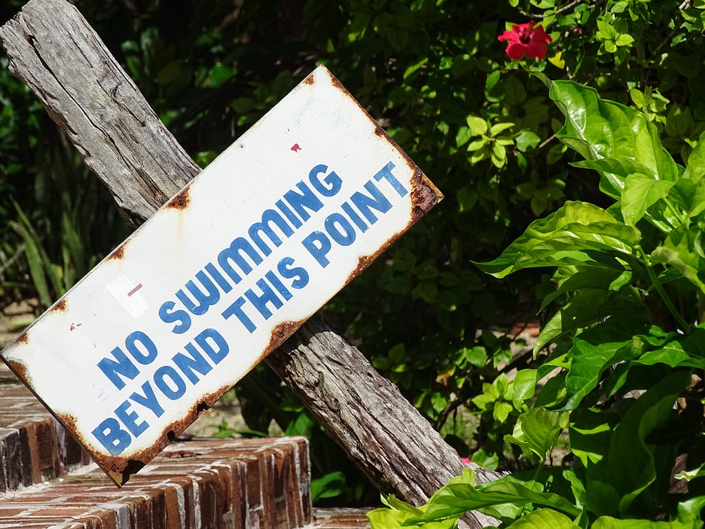 Photograph of a blue and white sign saying “No swimming beyond this point”