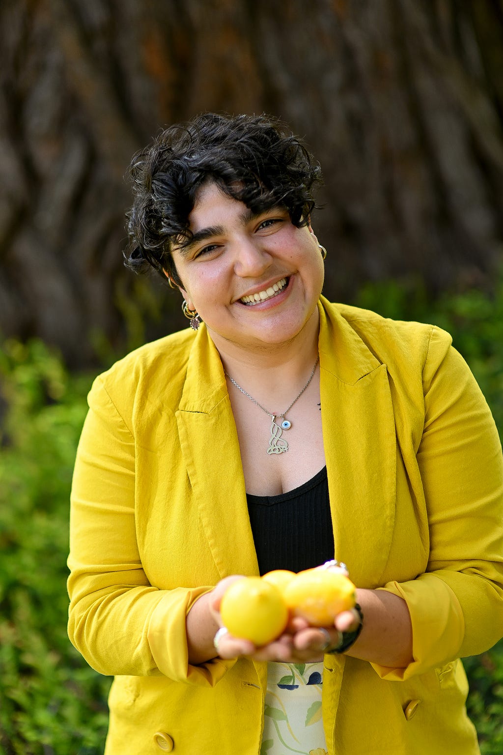 A person wearing a yellow jacket smile at the camera. They are holding lemons.