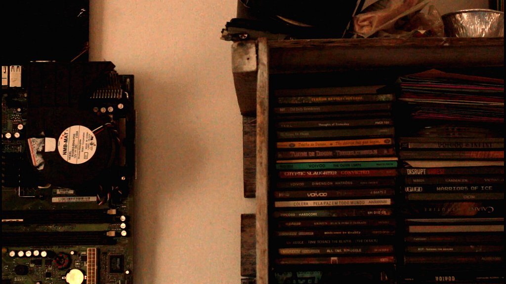 pecas de computador, cds empilhados dentro de um caixote preso na parede e objetos sobre o caixote.