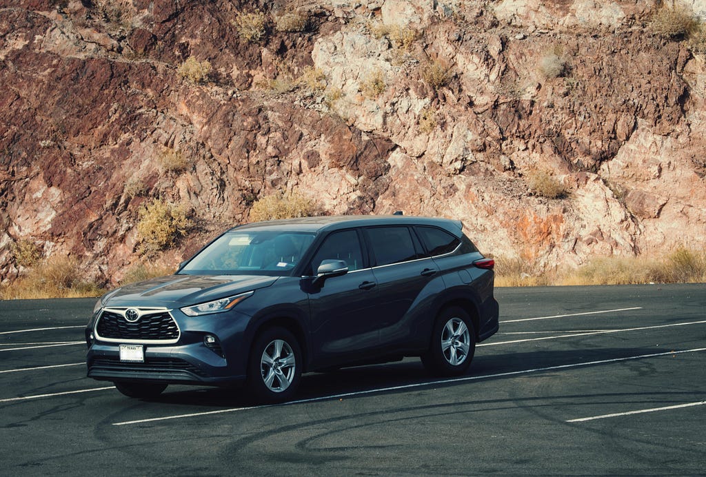 Dark gray 2022 Toyota Highlander in empty parking lot. Rocky hill the background.