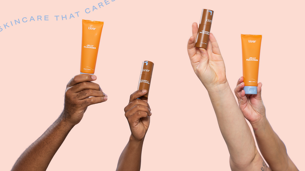 An image showcasing inclusivity, featuring four arms of different shades holding Kleer skincare products. Two arms are fair-skinned, one arm is olive-toned, and one arm is dark-skinned. The products held in the picture are a Kleer jelly cleanser tube and a Vitamin C moisturizer tube. The focus is on the diversity of the arms, indicating that the Kleer skincare line is designed for all skin types and shades. The image promotes inclusivity and celebrates diversity