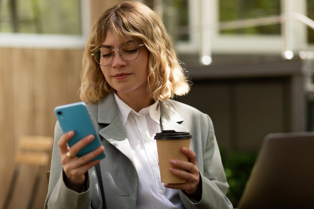 a woman uses her smartphone with one hand and the other hand holds coffee