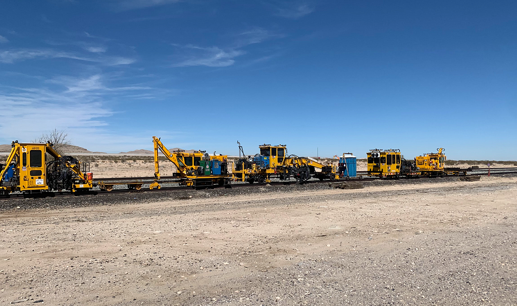 Four yellow freight company work equipment cars on train tracks